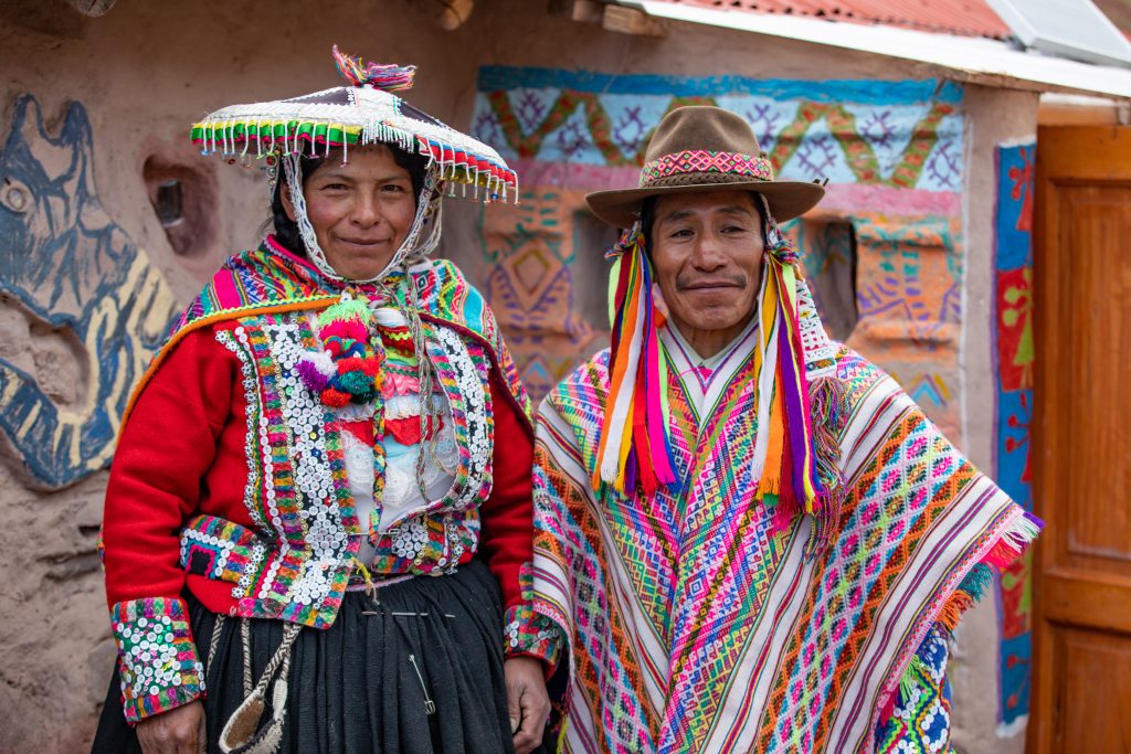 A Peruvian man and woman in traditional dress standing outside their home as part of a ADRA project.